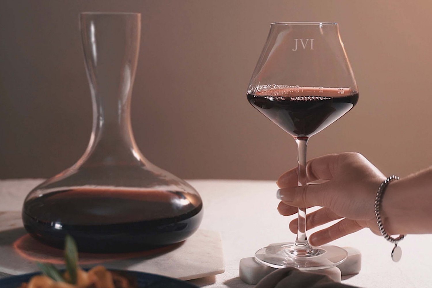 A wine decanter with red wine beside a red wine glass. the glass is personalised and engraved with initials JVI